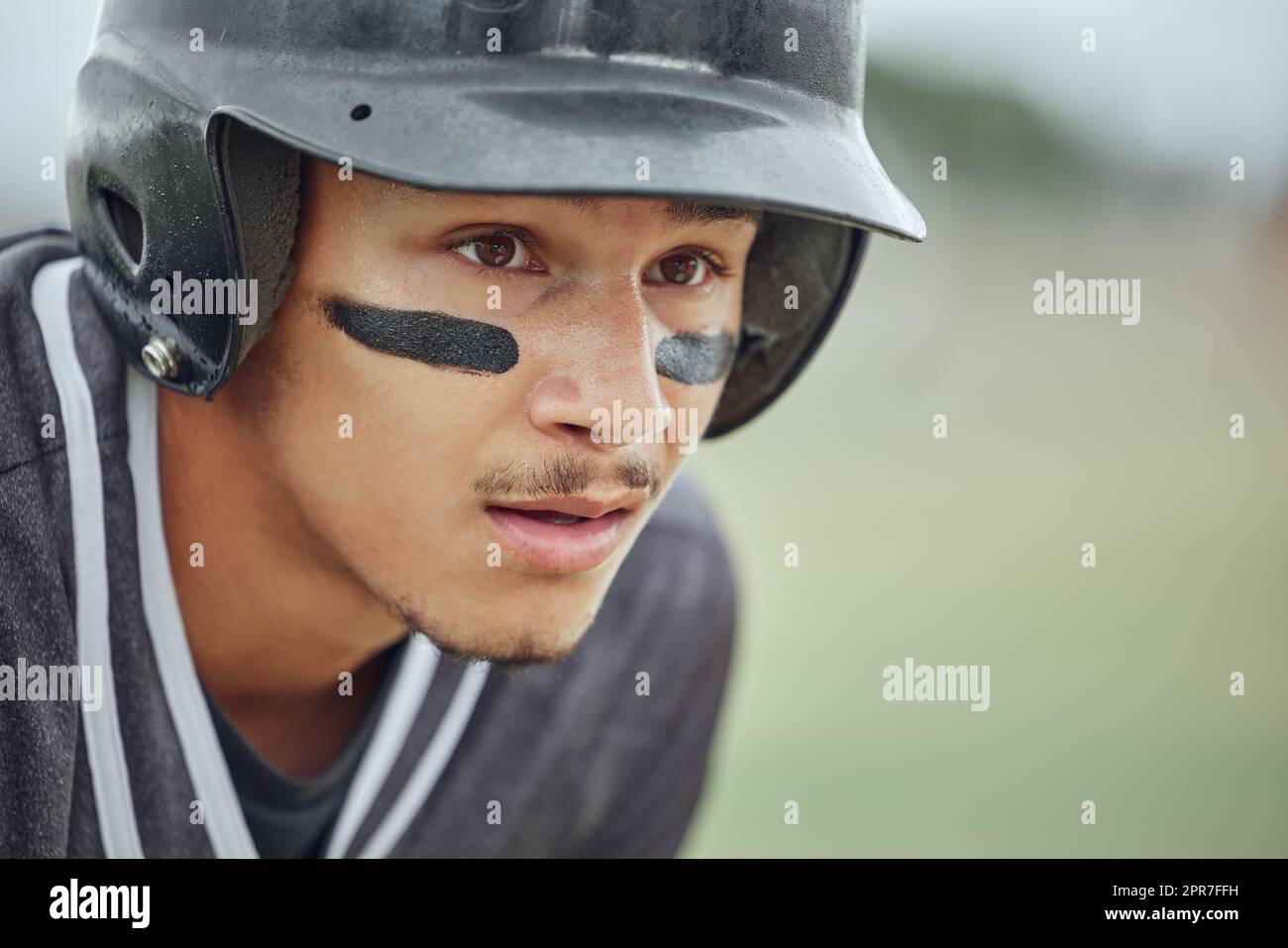 Closeup of baseball player looking focused with warrior paint on his face. Zoomed in on serious fit, active athlete wearing a helmet during a game on a pitch. Headshot of sporty man playing a match Stock Photo
