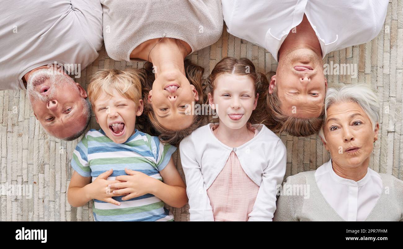 A family bonding together and being playful, showing different expressions while bonding and enjoying quality time. Above happy fun family making silly faces lying together on a living floor at home. Stock Photo