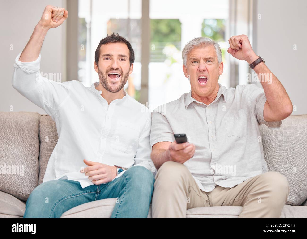 Come on. Cropped portrait of a handsome young man and his senior father cheering their team on while watching sports on the sofa at home. Stock Photo