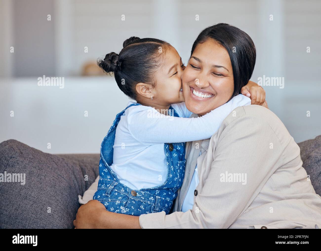 Adorable little mixed race girl kissing her mom on cheek while bonding at home. Loving, caring and affectionate mother and daughter spending quality time together. Woman being spoiled on mothers day Stock Photo