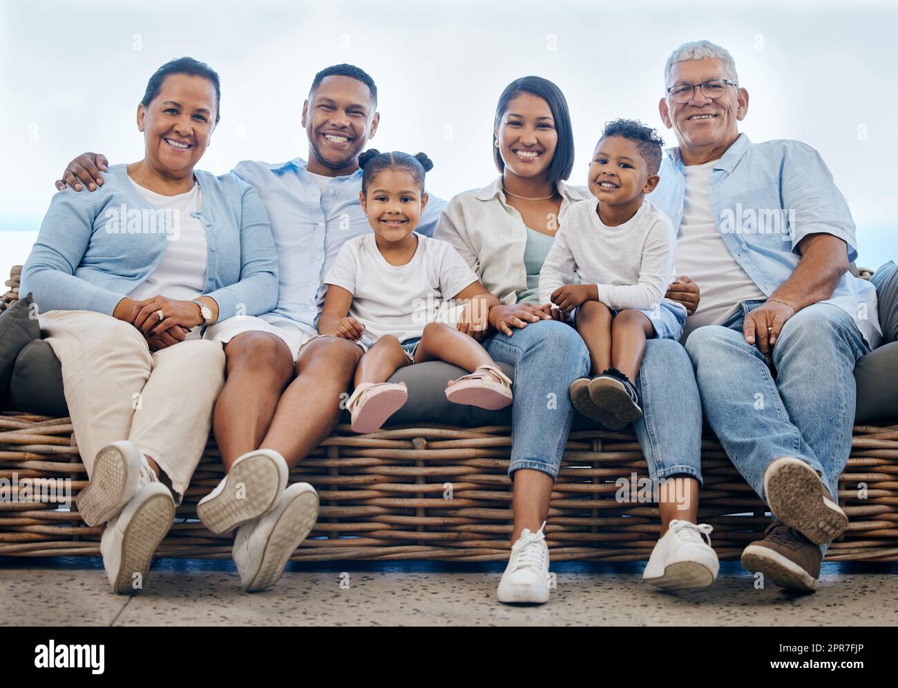 Happy and content hispanic family smiling while relaxing and sitting on the couch together at home. Cheerful and carefree little brother and sister enjoying time with their parents and grandparents Stock Photo