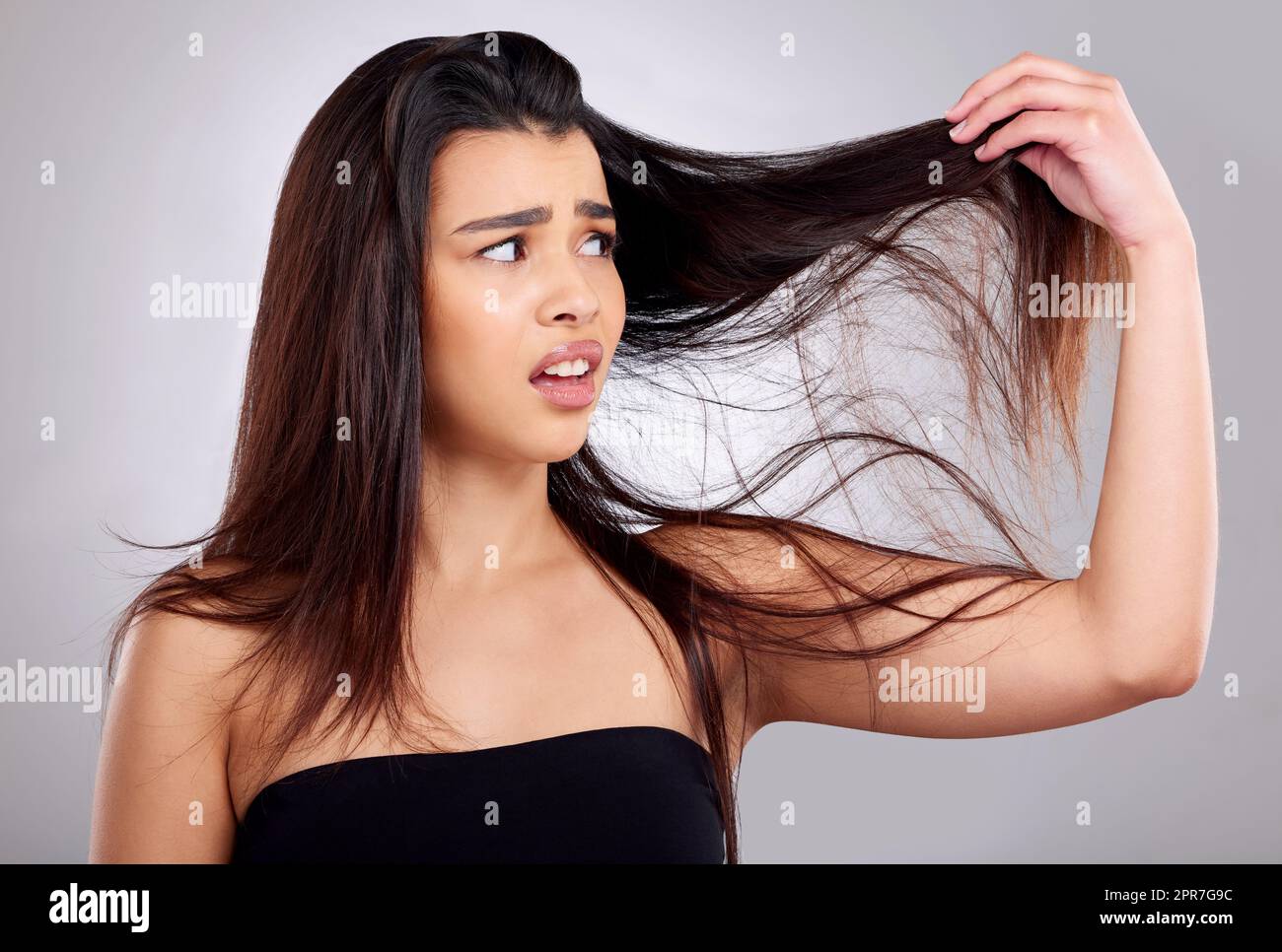 What is this. Studio shot of an attractive young woman having a bad hair day against a grey background. Stock Photo