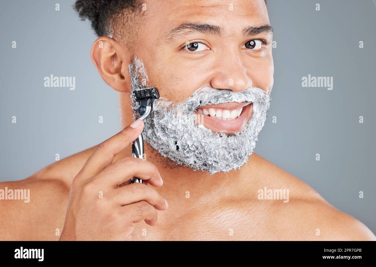 Lets get rid of this beard. Studio portrait of a handsome young man shaving against a grey background. Stock Photo