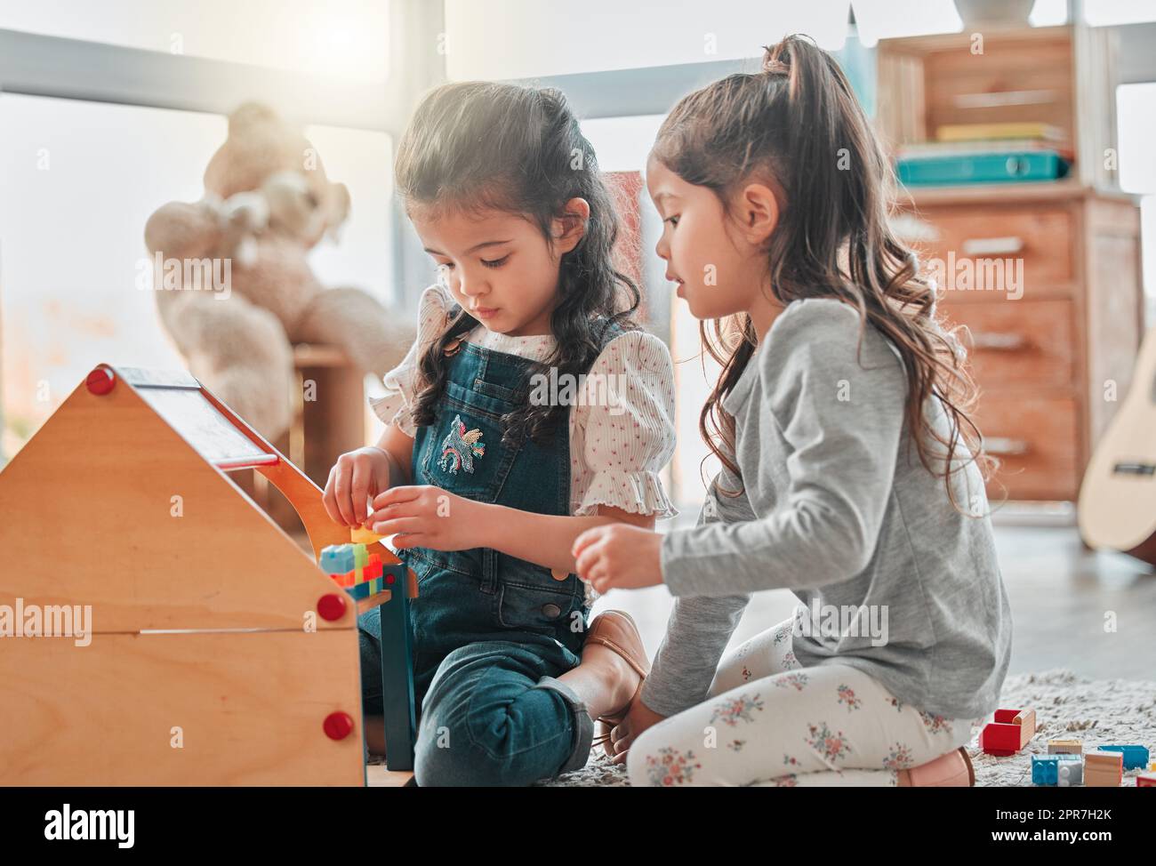 Were building a house for all our dolls to live in. two young girls playing with a dollhouse. Stock Photo