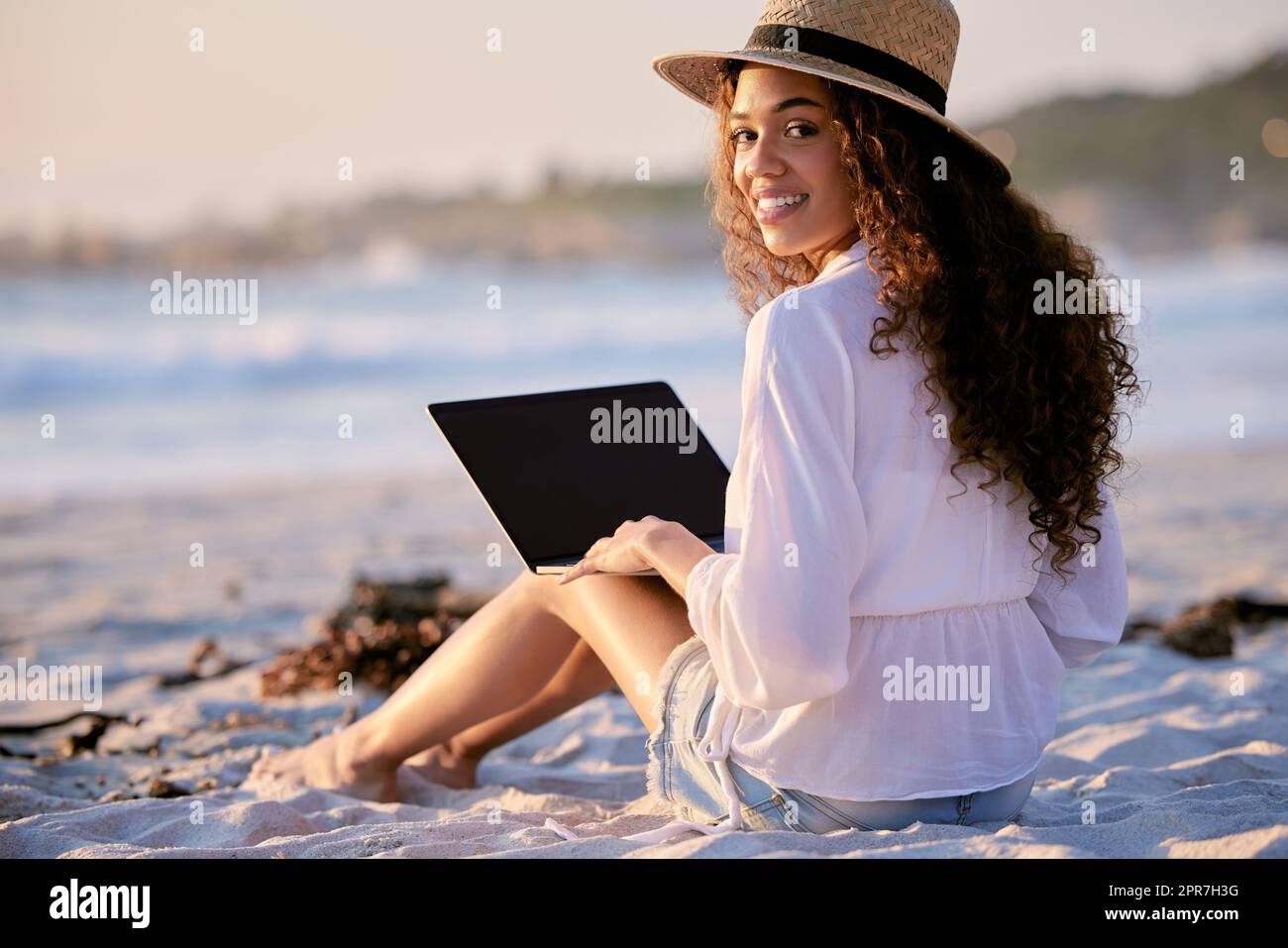 This place is perfect for anything. Portrait of a young beautiful woman using a laptop while sitting at the beach. Stock Photo