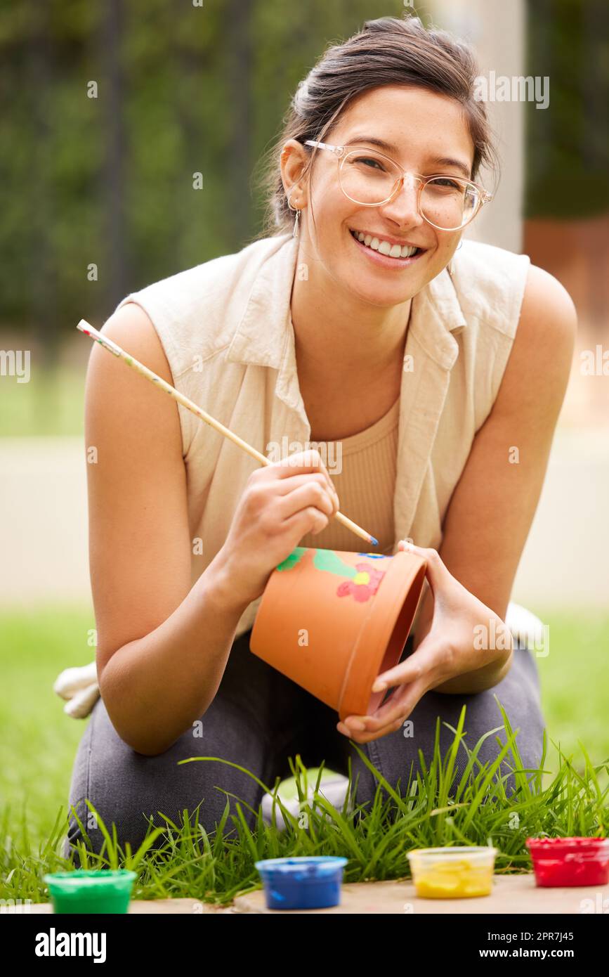 When learning is purposeful, creativity blossoms. s young woman painting a pot in the garden at home. Stock Photo