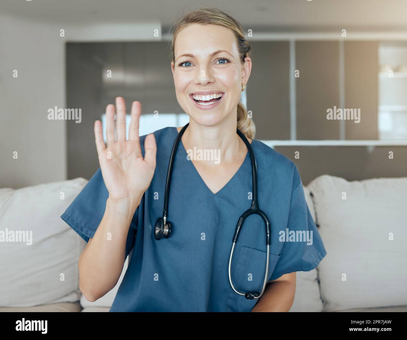 A beautiful young doctor looking happy and friendly while waiting on a sofa at work. Smiling caucasian health care worker talking and using hand gestures Stock Photo