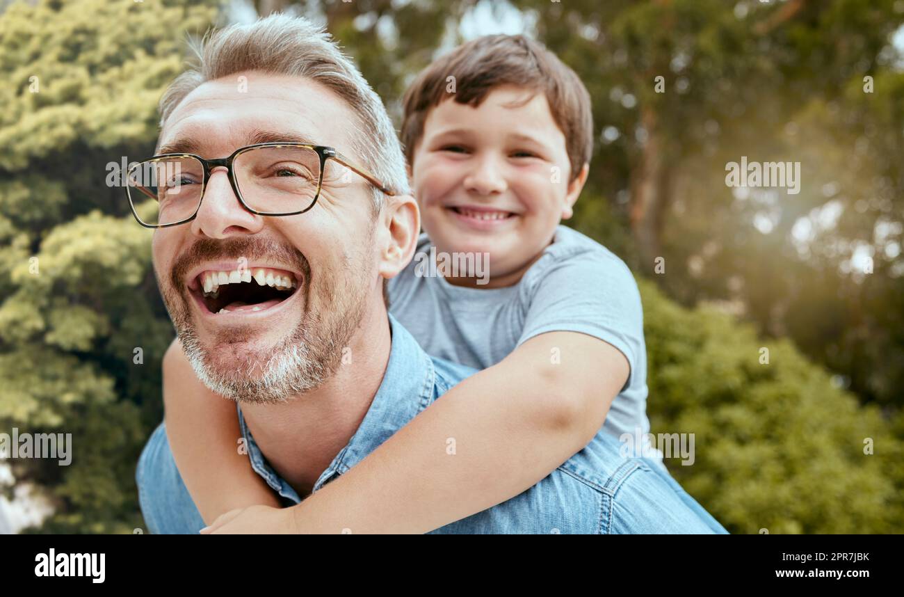 Happy caucasian father carrying playful little son on his back for piggyback ride in garden or backyard outside. Smiling parent bonding with adorable child. Kid enjoying relaxing free time with dad Stock Photo