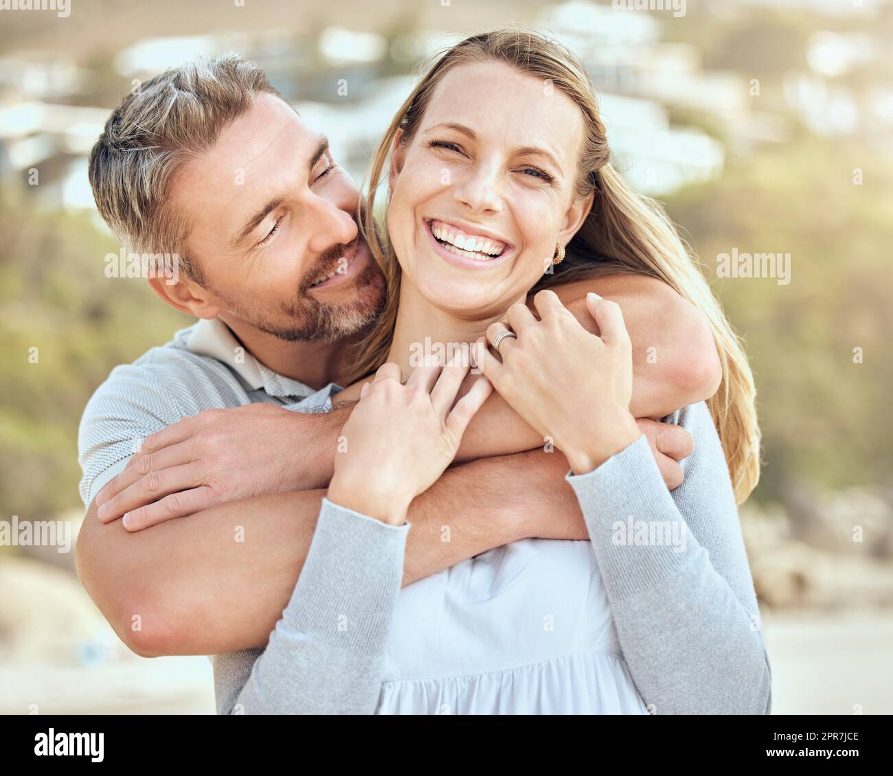 Happy and loving mature caucasian couple enjoying a romantic date at the beach together on a sunny day. Cheerful affectionate husband hugging arm around wife while bonding on vacation outdoors Stock Photo