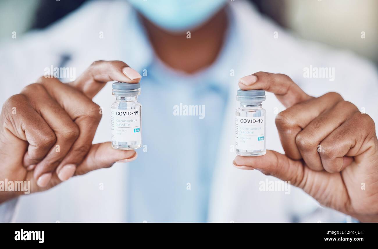 Closeup hand of african american woman doctor holding two bottles of the corona virus vaccine while standing in her hospital office. Be safe during the pandemic outbreak. Stop the spread of covid 19 Stock Photo