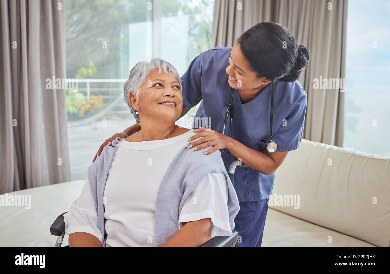 A hispanic senior woman in a wheelchair and her female nurse in the old age home. Mixed race young nurse and her patient in the lounge Stock Photo