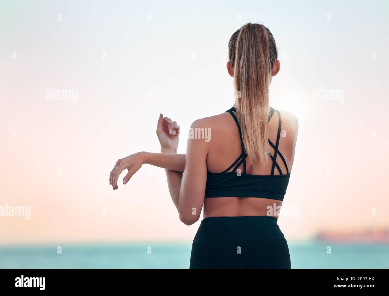 Rearview beautiful woman practising yoga exercise on the beach. Young female athlete stretching and warming up while working out outside. Finding inner peace and balance. Health and lifestyle Stock Photo