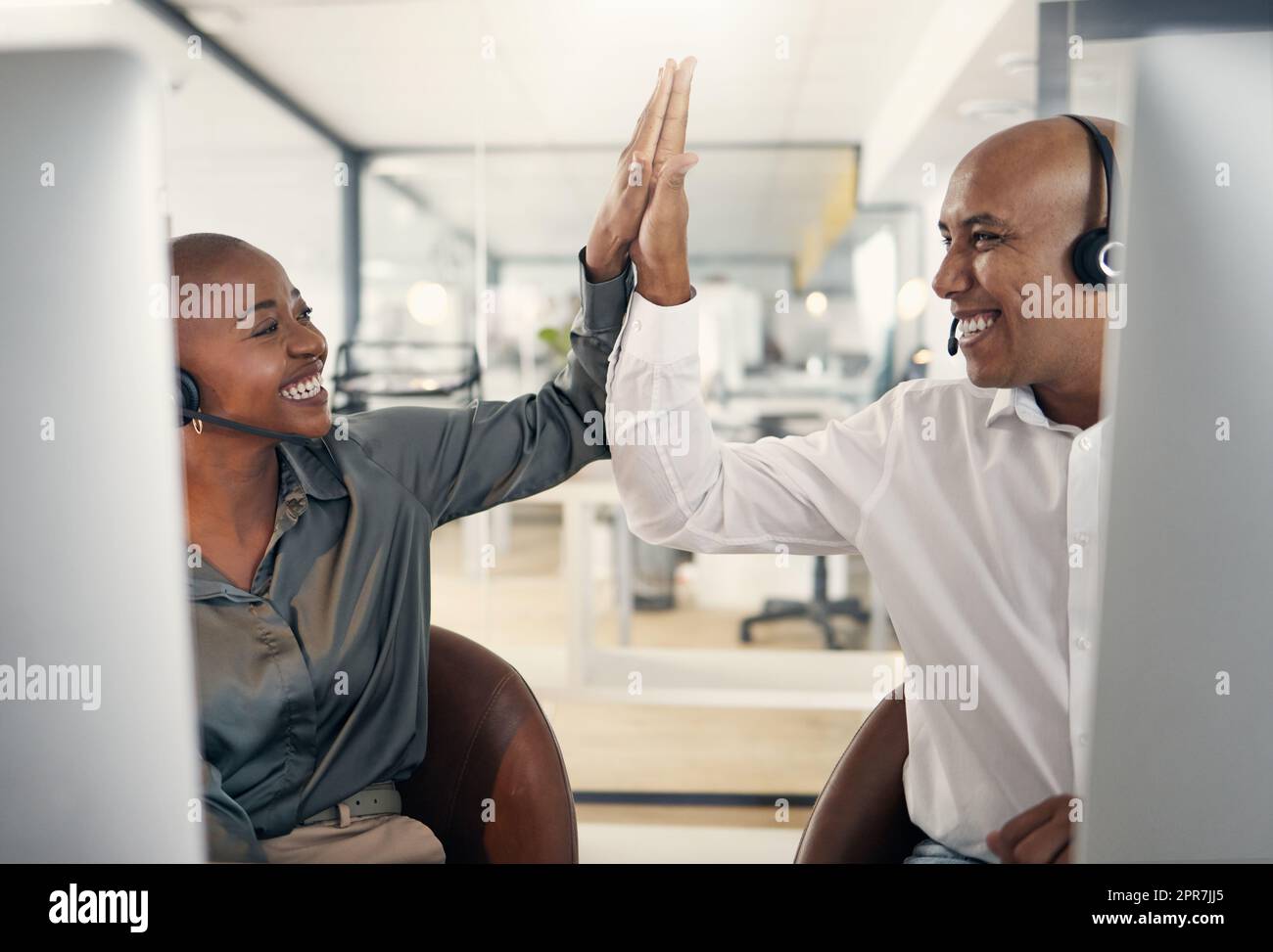 Two happy call centre telemarketing agents giving each other high five and cheering with joy while working in an office. Excited and ambitious consultants celebrating successful sales targets and winning victory Stock Photo