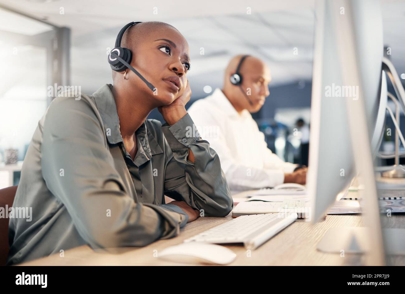 Stressed african american call centre telemarketing agent looking bored and anxious while working on broken computer in an office. Worried female consultant having problems with slow internet connection error. Lazy employee struggling with difficult calle Stock Photo