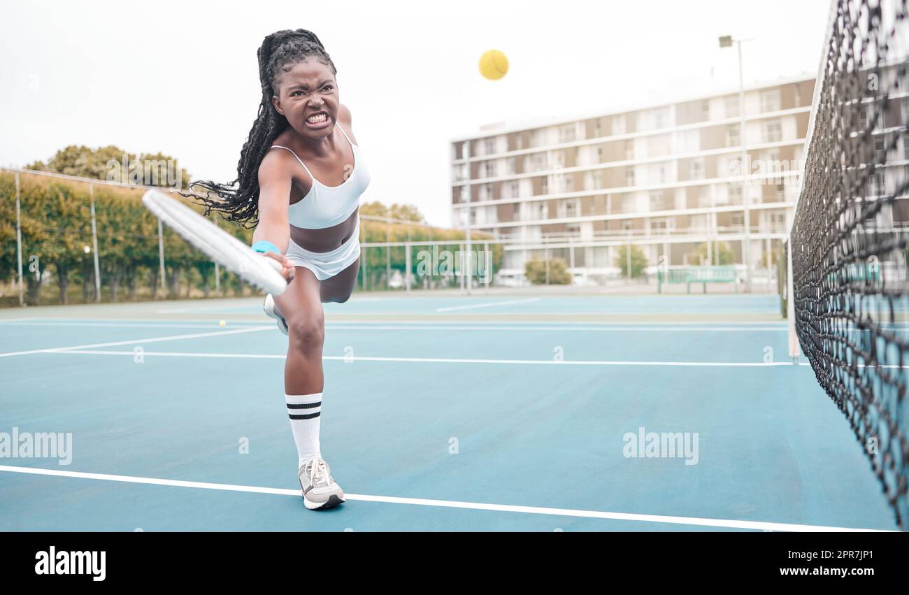 Strong tennis player hitting a ball during a match. Young girl making a facial expression during a game of tennis. Angry tennis player competing in fun tennis practice. Healthy woman playing tennis Stock Photo