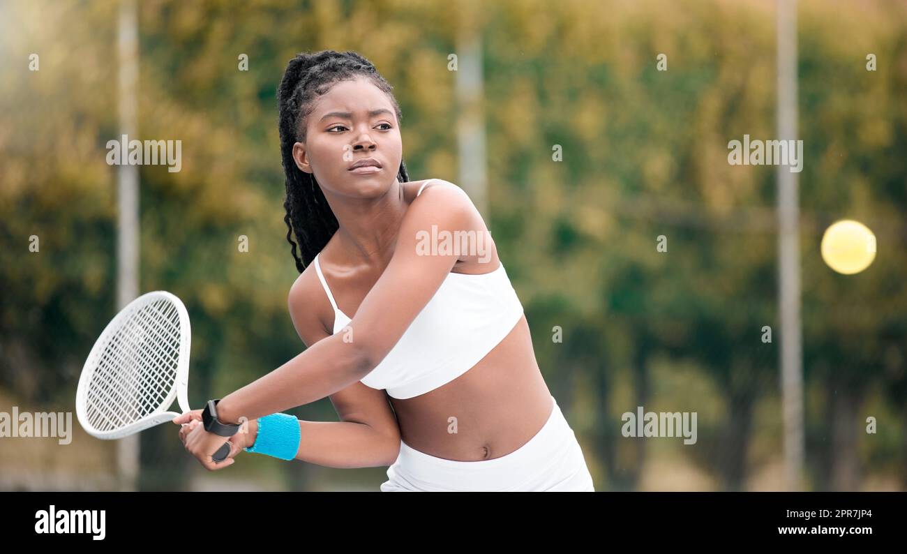 Young girl waiting to hit a ball in a tennis match. African american woman enjoying a game of tennis. Serious young woman playing tennis on her club court. Active, fit player hitting a tennis ball Stock Photo