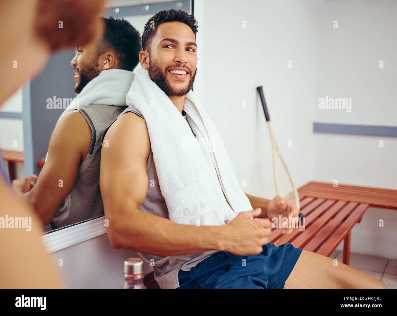 Fit athlete sitting on a bench talking to his friend. Two friends taking a break in the gym. Players bonding and talking before a match. Professional players before a game practice Stock Photo