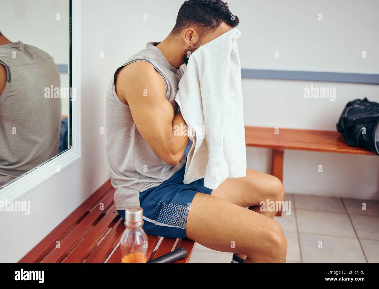 Young player wiping his face with a towel. Tired man cleaning his face with a towel after a squash match. Squatch player sitting in his gym locker room. Mixed race man taking a break after a match Stock Photo