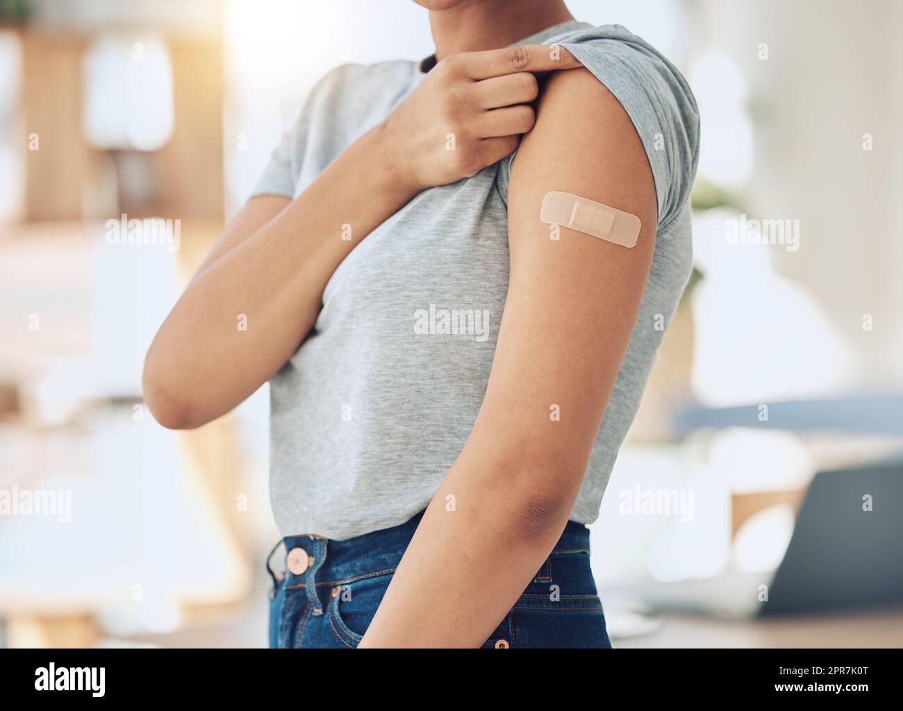 Closeup of mixed race woman wearing a bandaid plaster on her arm after getting a covid vaccine shot at a clinic or hospital. One female only strengthening immunity from flu and disease to stay healthy Stock Photo