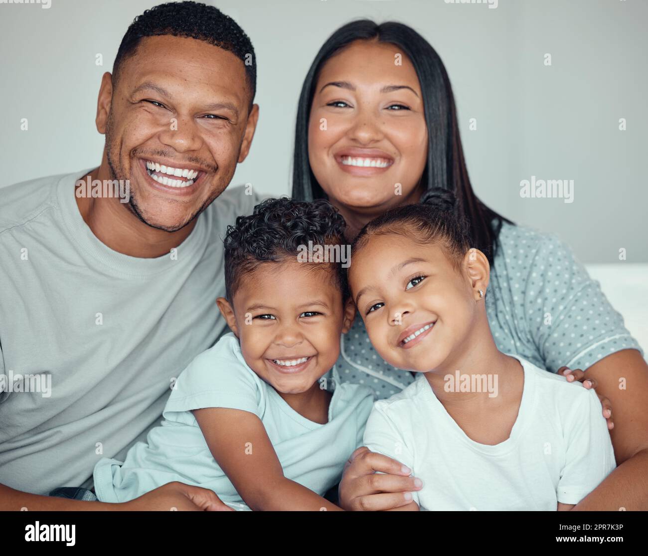 Portrait of a happy young mixed race family with two children wearing pyjamas and sitting at home together. Loving little sister and brother spending time with their parents on the weekend Stock Photo