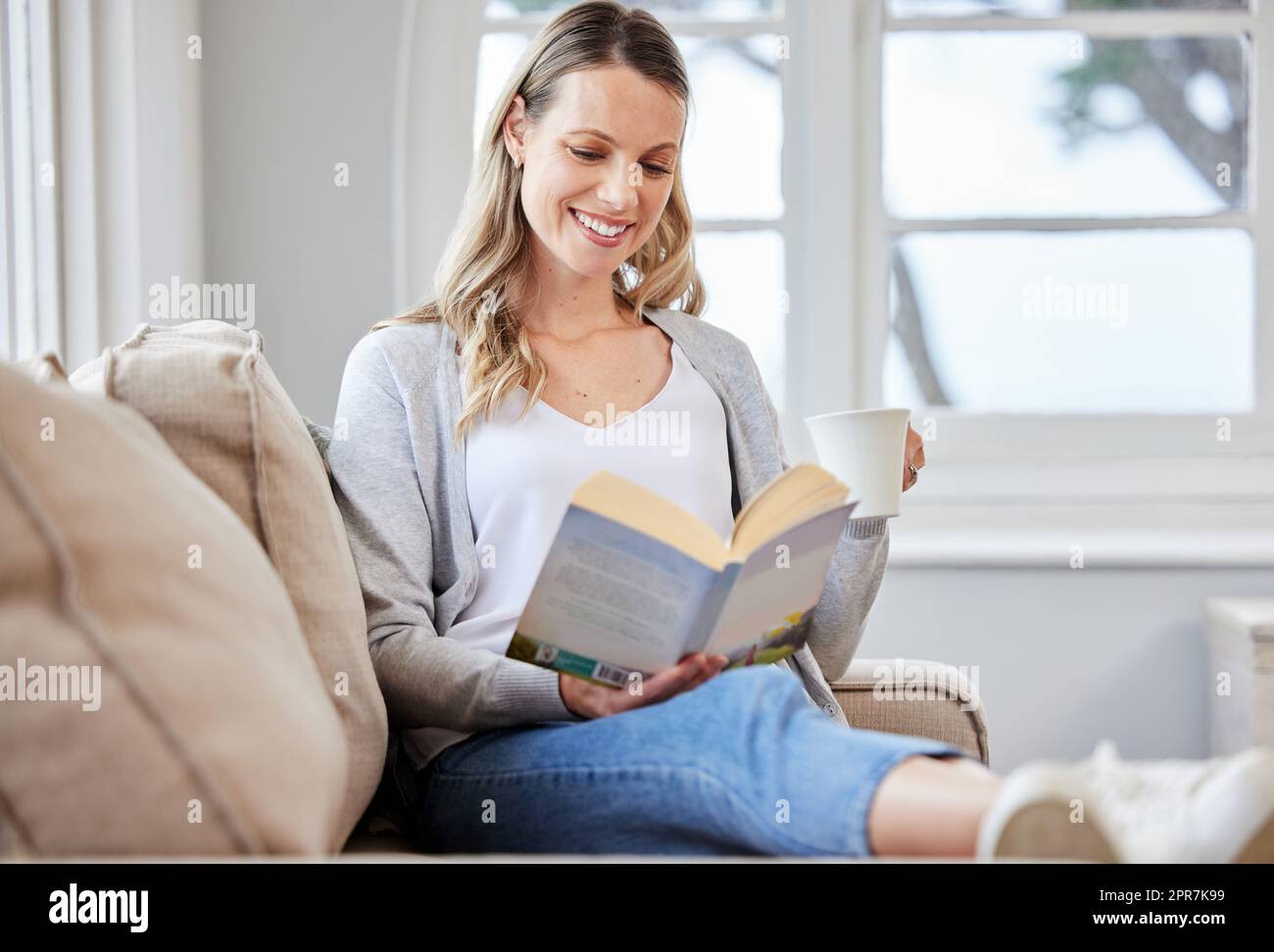 A good book leads to a good mood. a young woman reading a book while relaxing on a sofa at home. Stock Photo