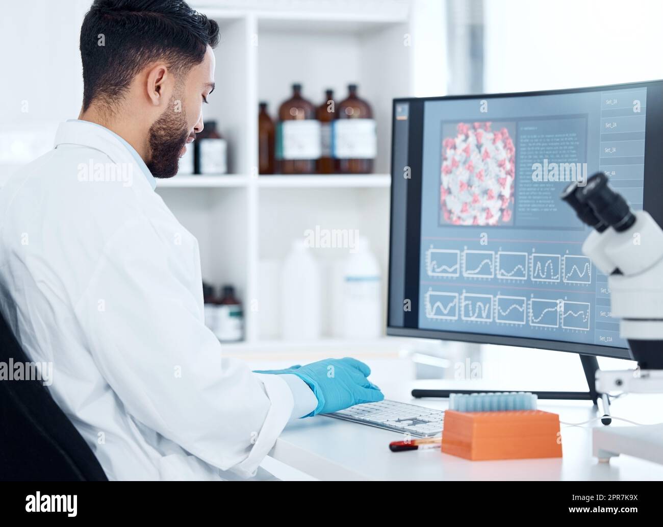 One mixed race scientist from the back analysing medical test samples and data from microbiology and genetic research on computer screen in lab. Young man developing cure for virus with biotechnology Stock Photo