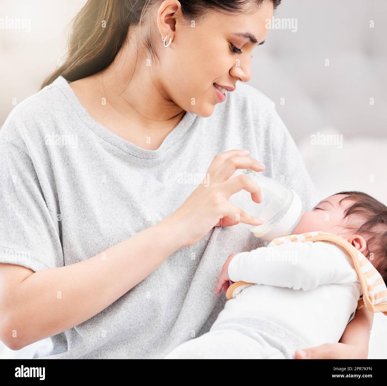 Young hispanic mother feeding her newborn baby a milk bottle and