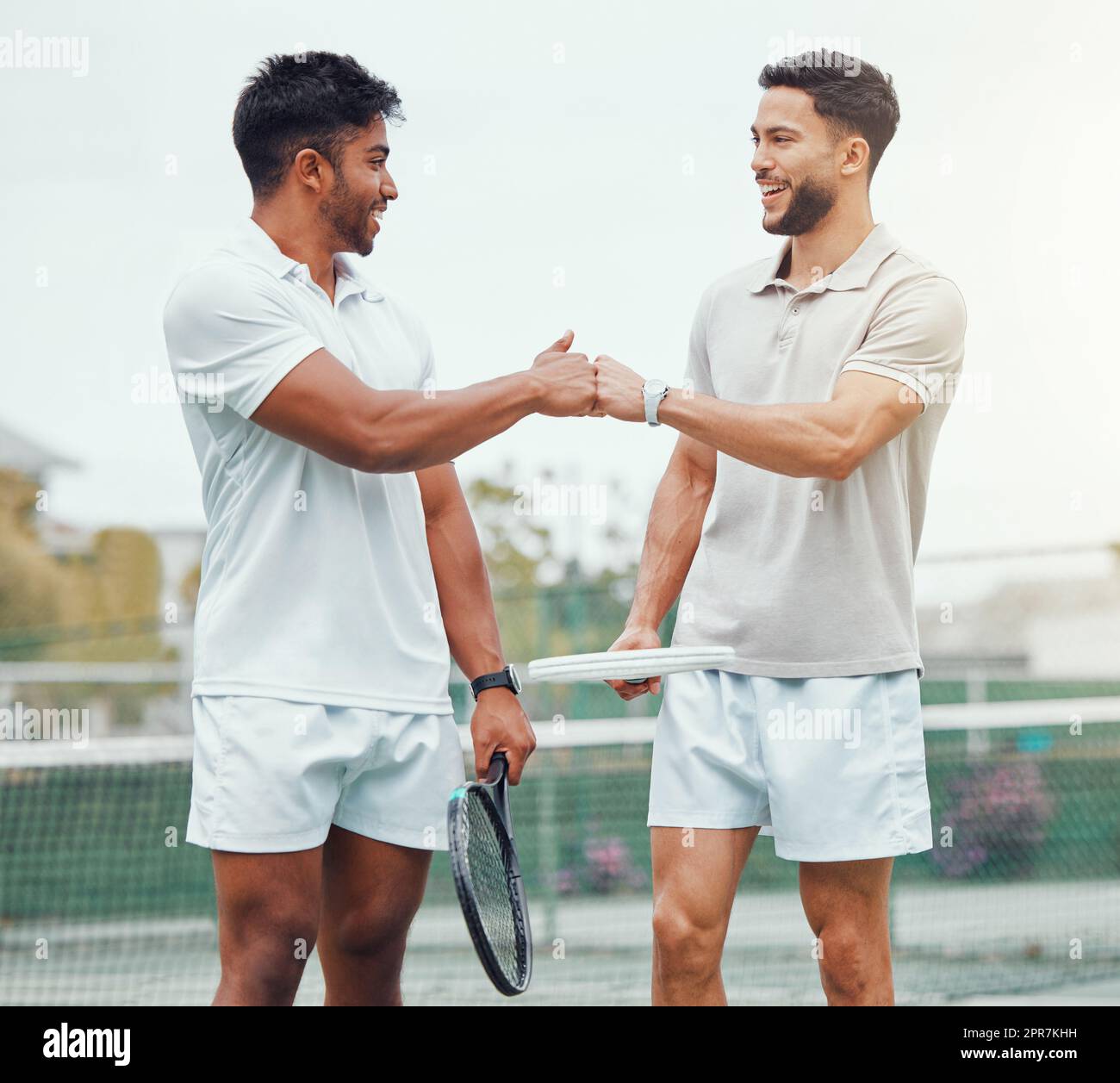 Two smiling ethnic tennis players giving fistbump with fist before playing court game. Fit athletes team standing and using hand gesture for good luck. Play competitive sports match for health fitness Stock Photo
