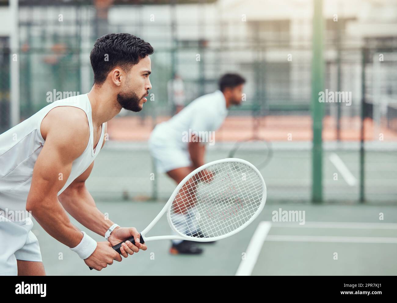 Two ethnic tennis players holding rackets and ready to play court game. Serious, focused athletes together in stance. Playing competitive doubles match as team to stay fit and healthy in sports club Stock Photo
