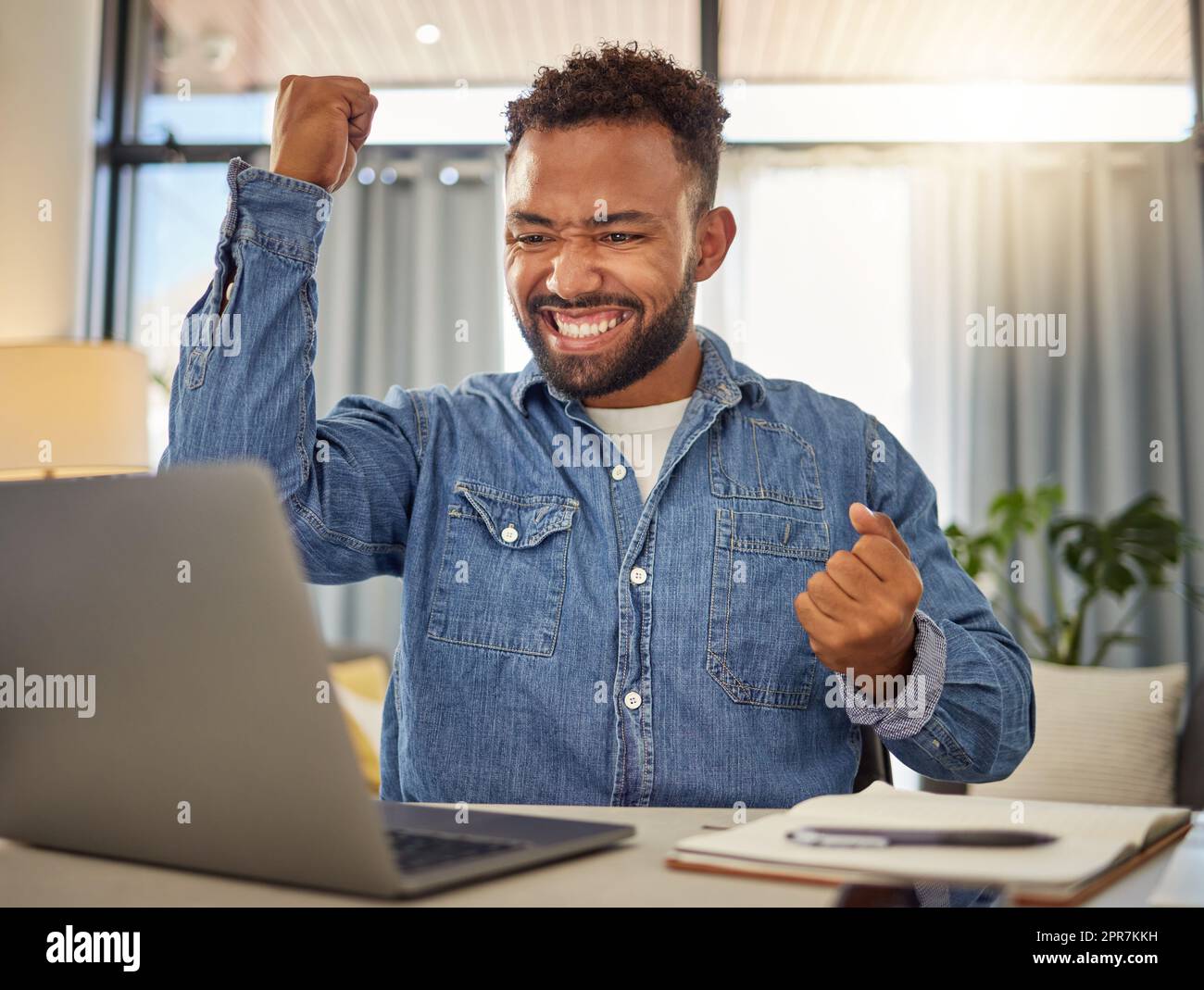 Excited businessman cheering for his success. Cheerful entrepreneur cheering after reading an email on his laptop. Virtual remote businessman in luck after using his computer Stock Photo