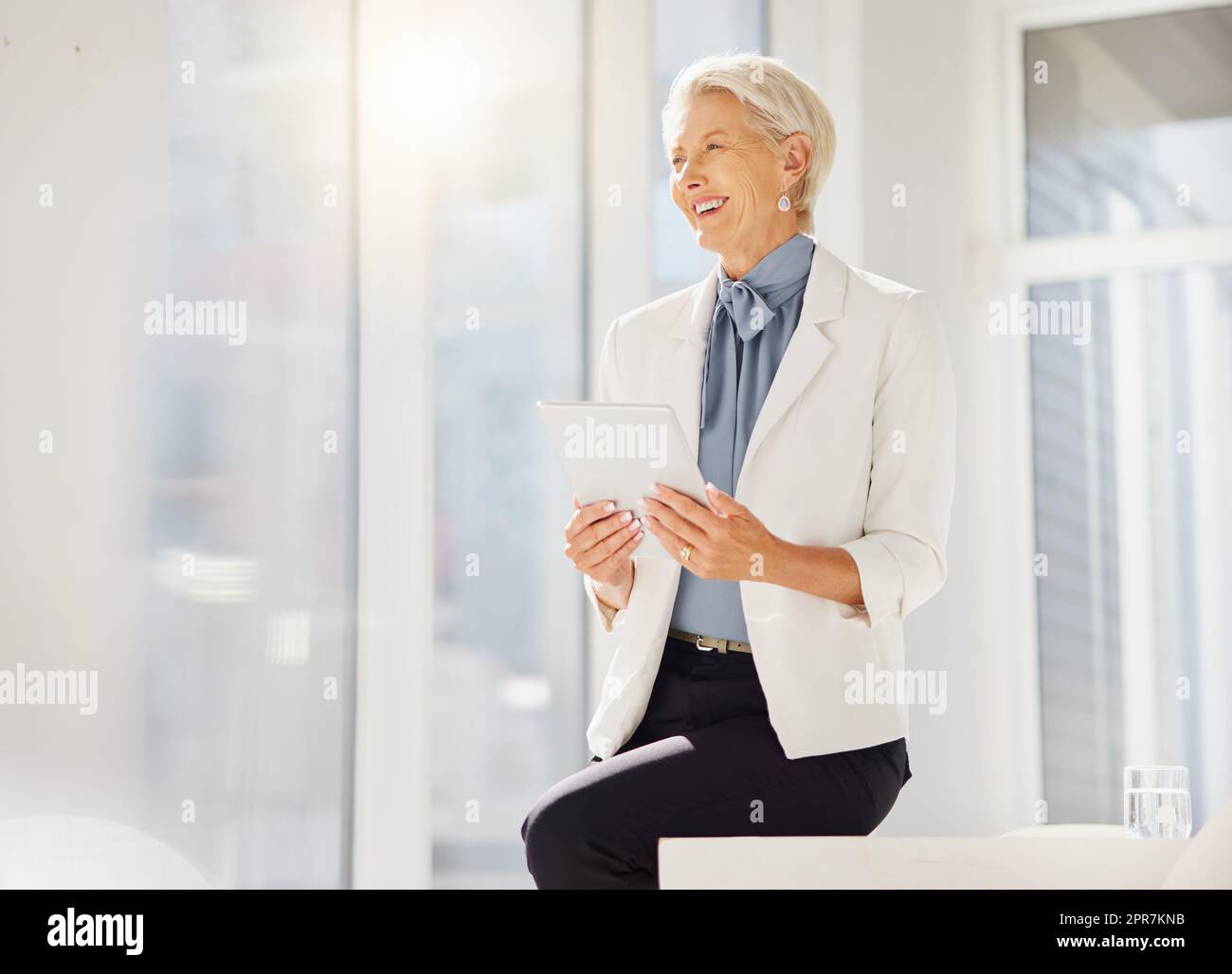 One confident thoughtful mature caucasian businesswoman planning on a digital tablet device in an office. Successful entrepreneur and dedicated leader with grey hair smiling and thinking of ideas while searching the internet for inspiration in her startup Stock Photo