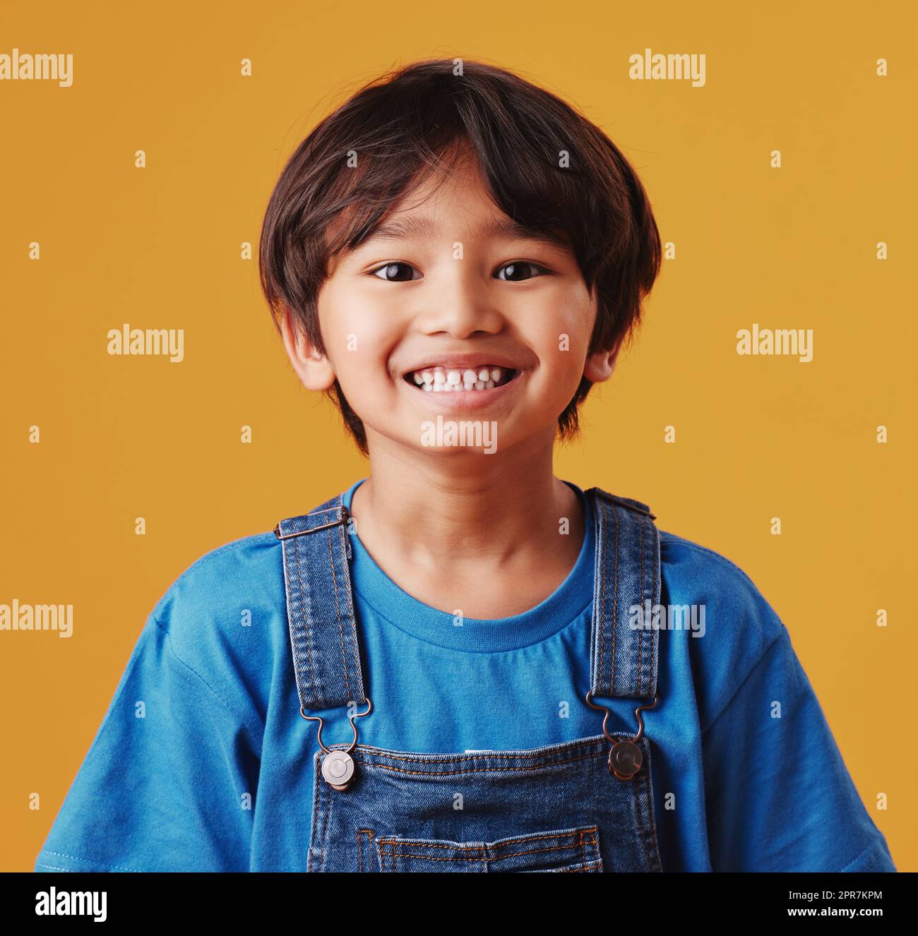 Portrait of a cute little asian boy wearing casual clothes while smiling and looking excited. Child standing against an orange studio background. Adorable happy little boy safe and alone Stock Photo