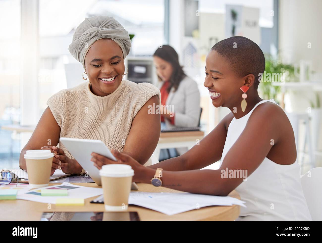 Smiling african american business women sitting together and using a digital tablet during a brainstorm meeting in the office. Confident happy black professionals planning a strategy with technology Stock Photo