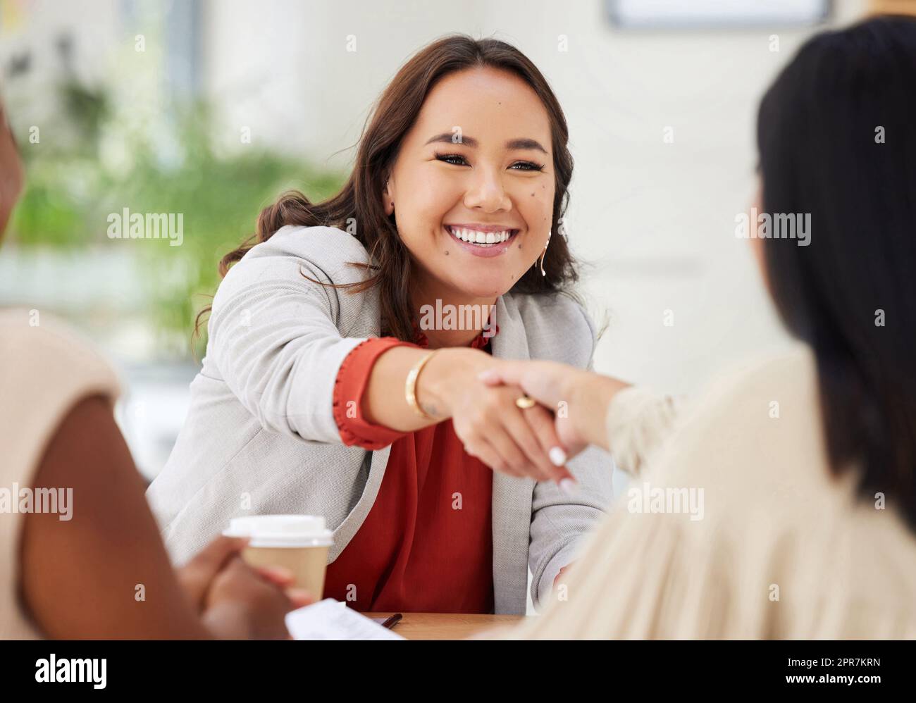 Team of smiling diverse business women shaking hands in office after meeting in boardroom. Group of happy professionals and colleagues using handshake and gesture to congratulate success and welcome Stock Photo