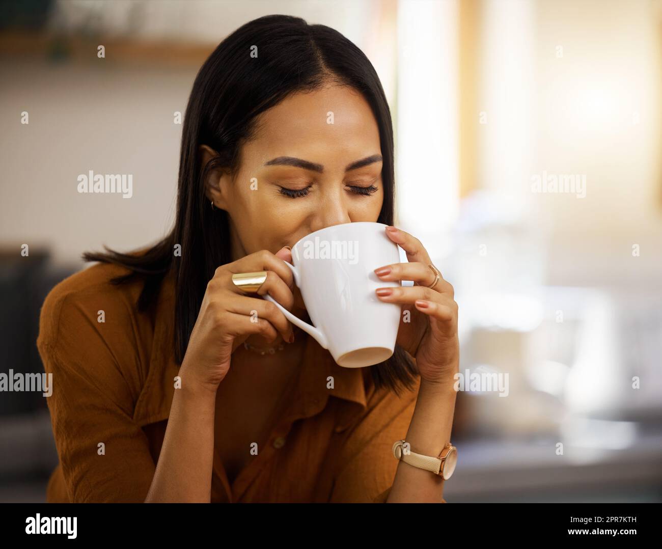 Young happy beautiful mixed race woman enjoying a cup of coffee alone at home. Hispanic female in her 20s drinking a cup of tea in the kitchen at home Stock Photo