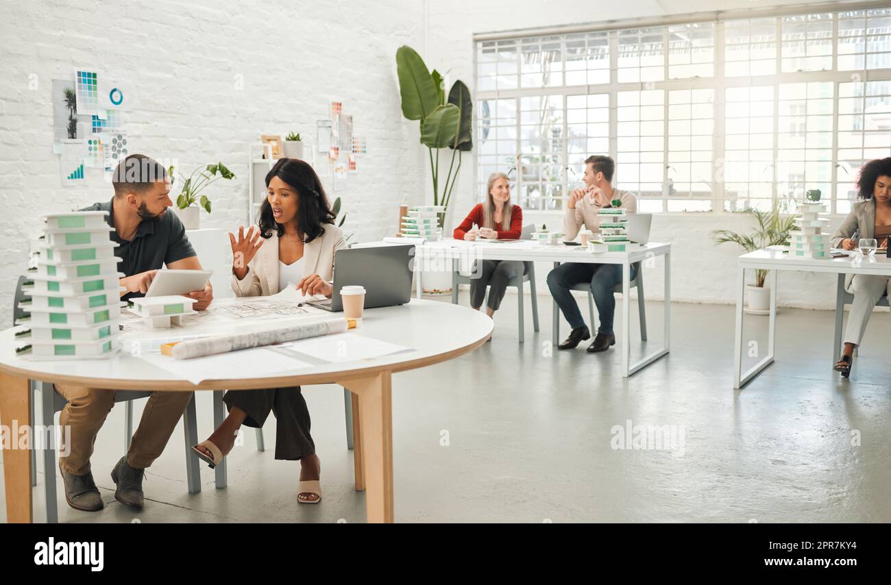 Businesspeople collaborate on a building project. Colleagues talking about building blueprint. Diverse businesspeople working together. Businesspeople planning in a modern office Stock Photo