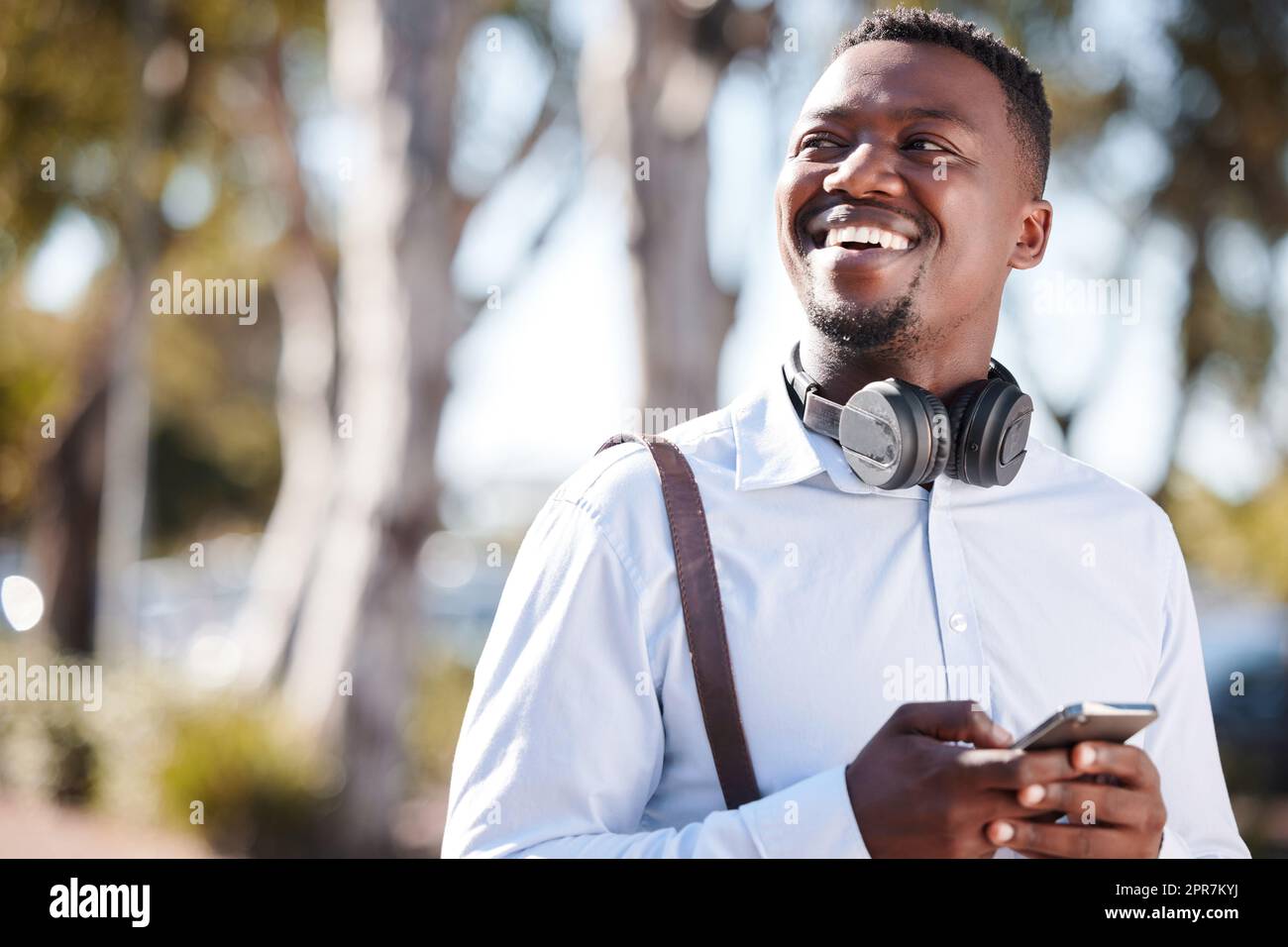 Happy african american businessman wearing headphones and texting on a cellphone while commuting in the city. One young black guy looking thoughtful while using apps and browsing social media online Stock Photo