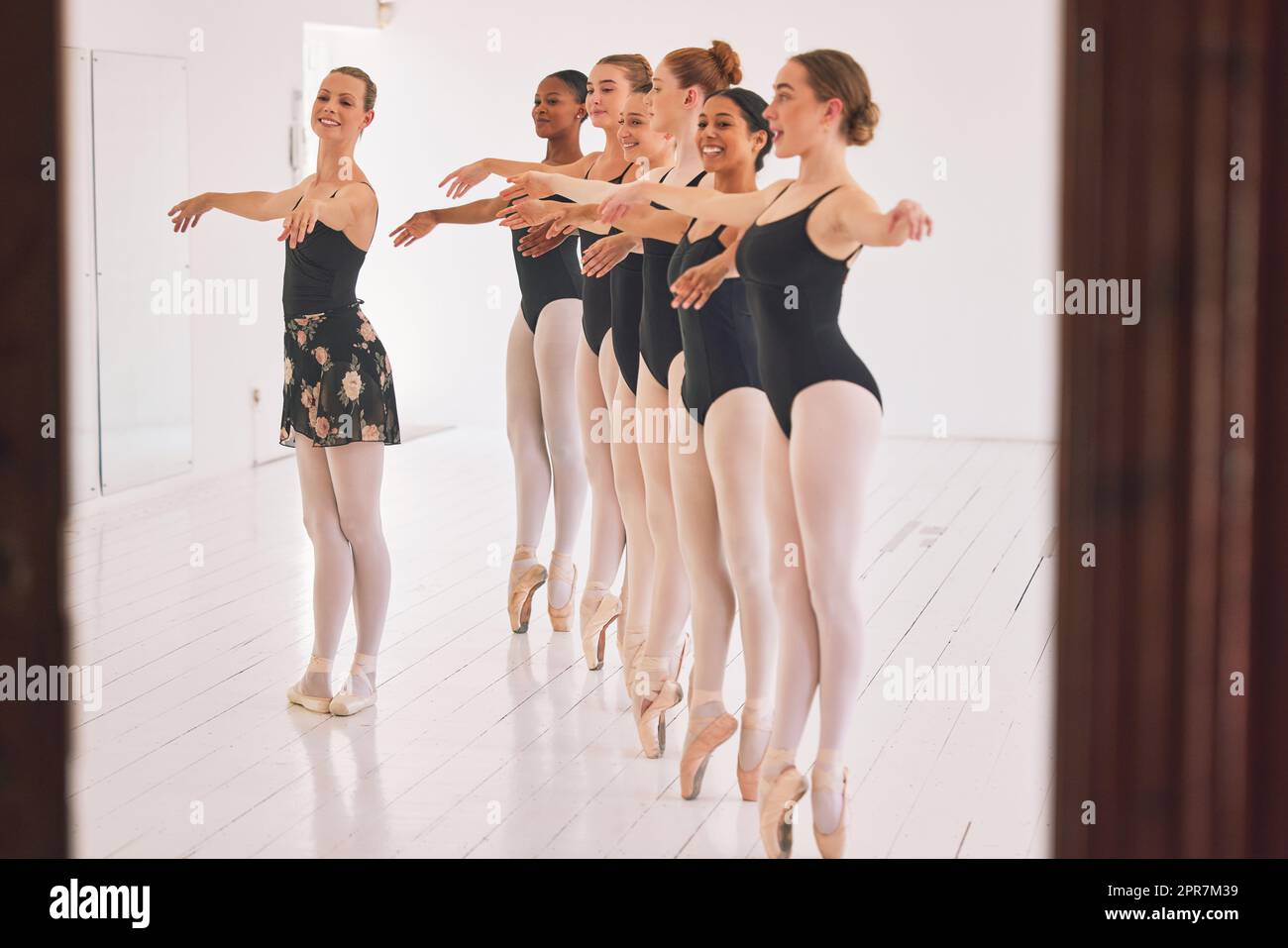 Young woman dance instructor teaching a ballet class to a group of a children in her studio. Ballerina teacher working with girl students, preparing for their recital, performance or upcoming show Stock Photo