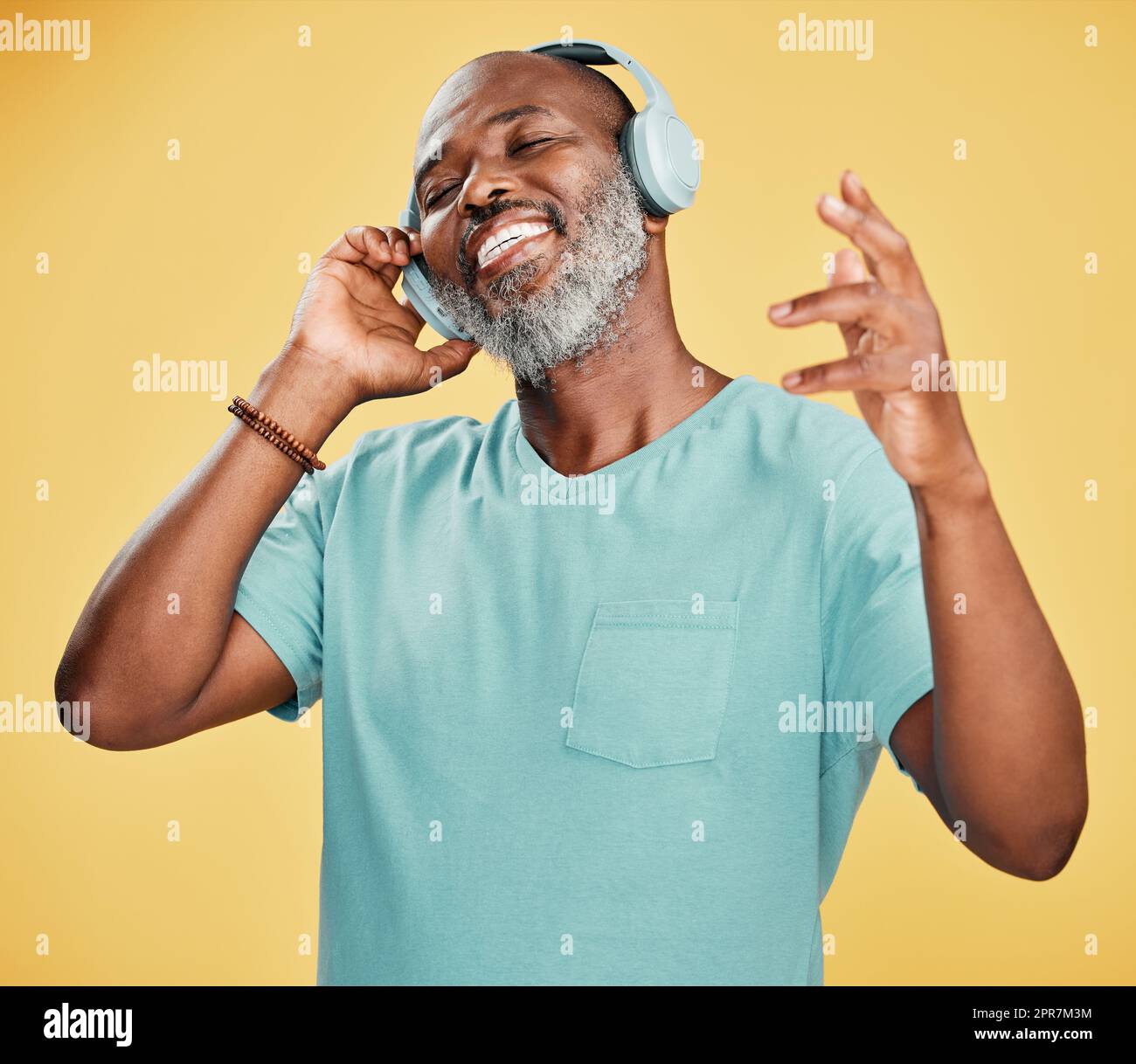 One happy mature African American man wearing headphones and listening to music while dancing against a yellow background in the studio. Smiling black man feeling free while expressing through dance Stock Photo