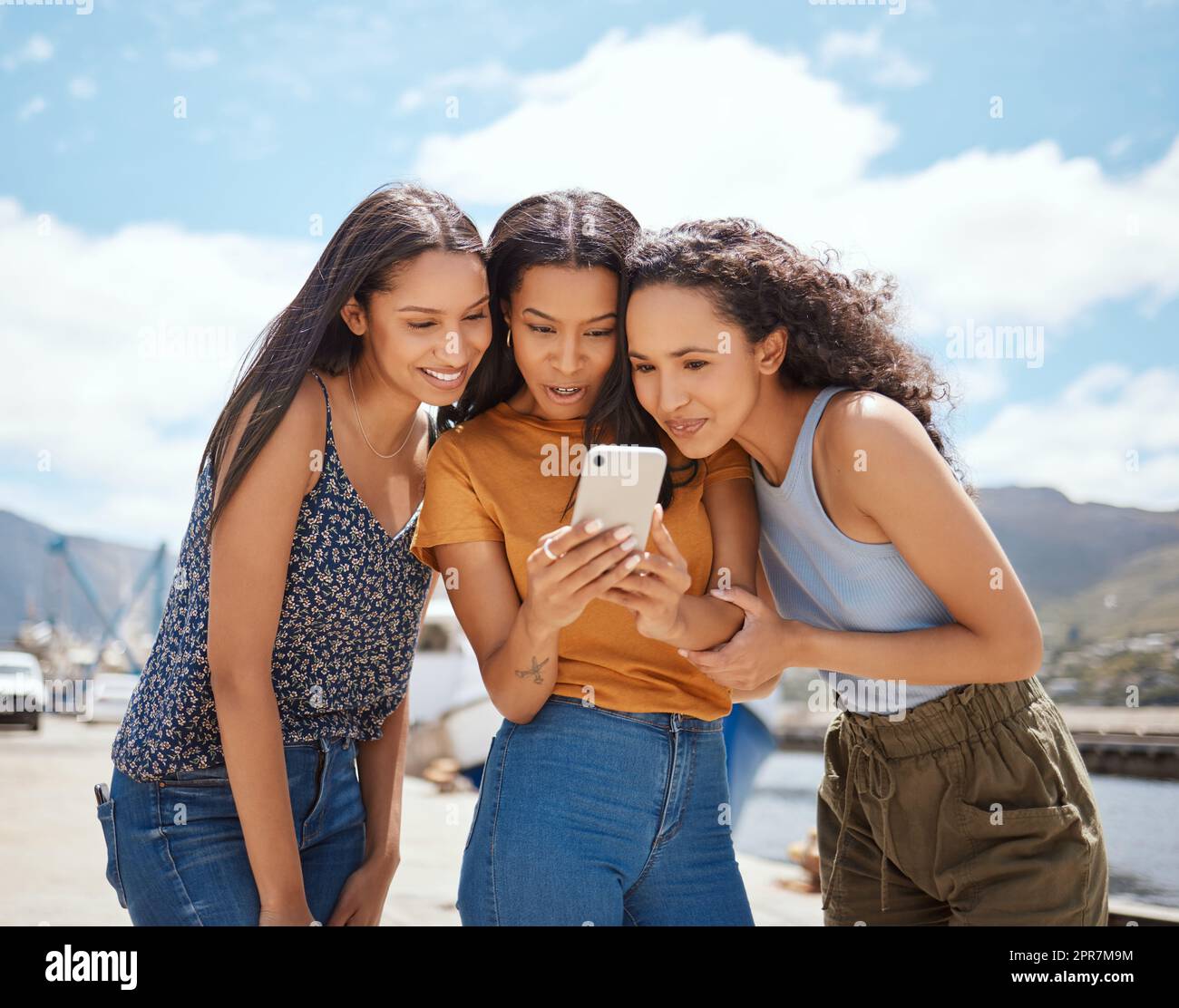 Lets watch it together. a group of women looking at something on a cellphone together outdoors. Stock Photo