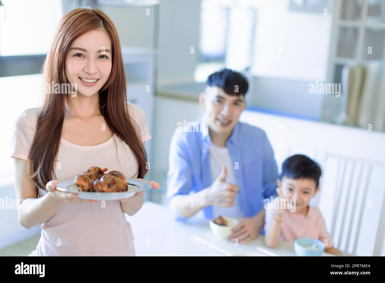 Mother showing tasty food and father showing thumbs up. Happy Asian  family having dinner at home Stock Photo