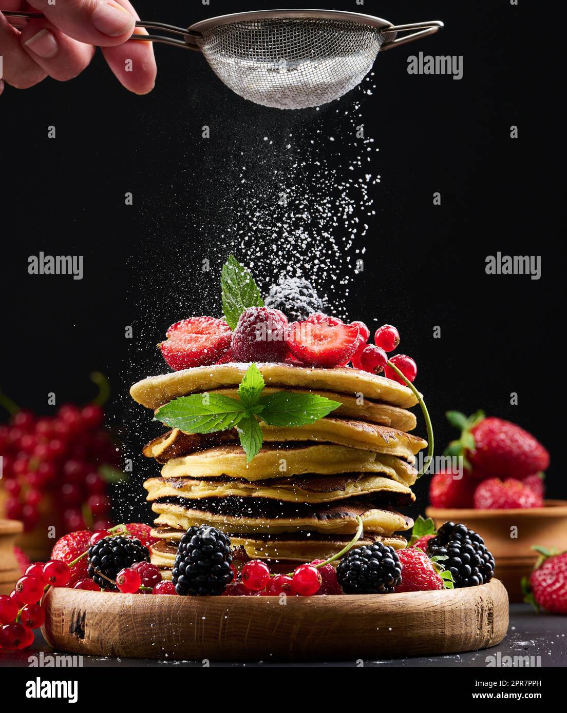 A stack of pancakes with fresh fruit sprinkled with powdered sugar on a black background Stock Photo