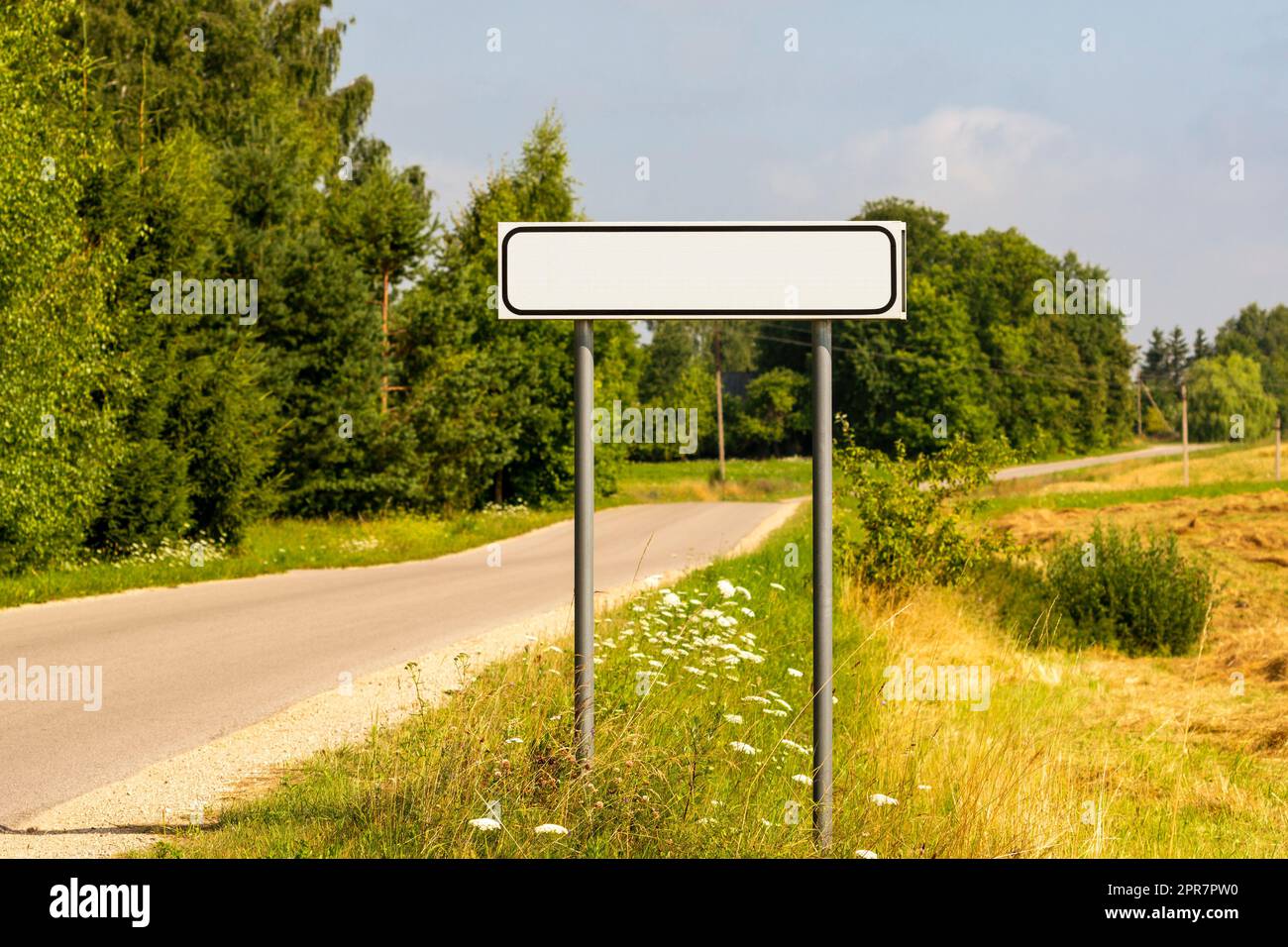 Asphalt road with white empty sign on roadside at city entrance Stock Photo