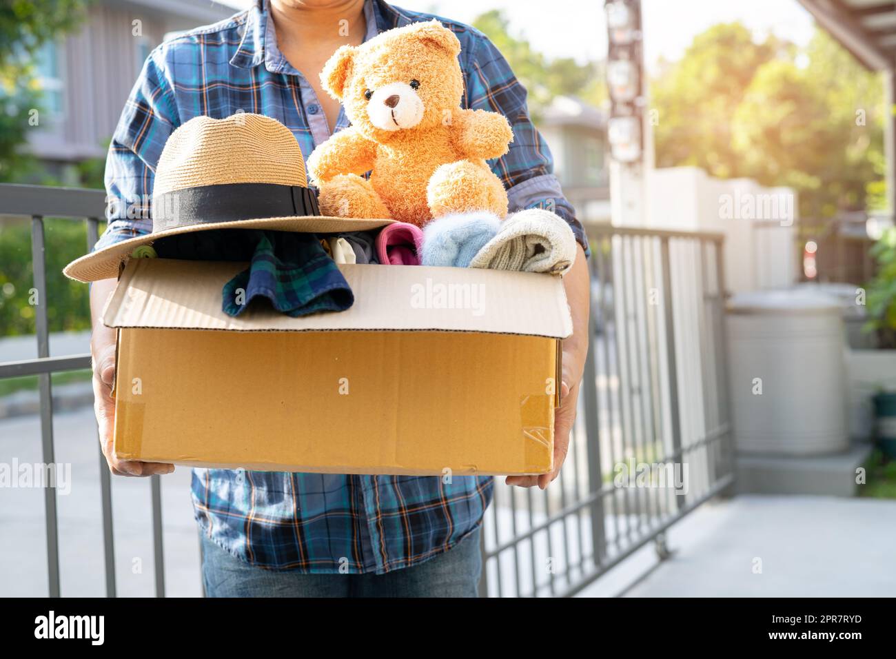 Holding clothing donation box with used clothes and doll at home to support help for poor people in the world. Stock Photo