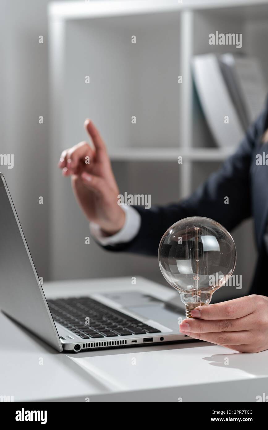Businesswoman Pointing Recent Updates With One Finger On Desk Holding Lightbulb. Woman In Office Showing Important Message On Computer. Executive Presenting Crutial Data Into Pc. Stock Photo
