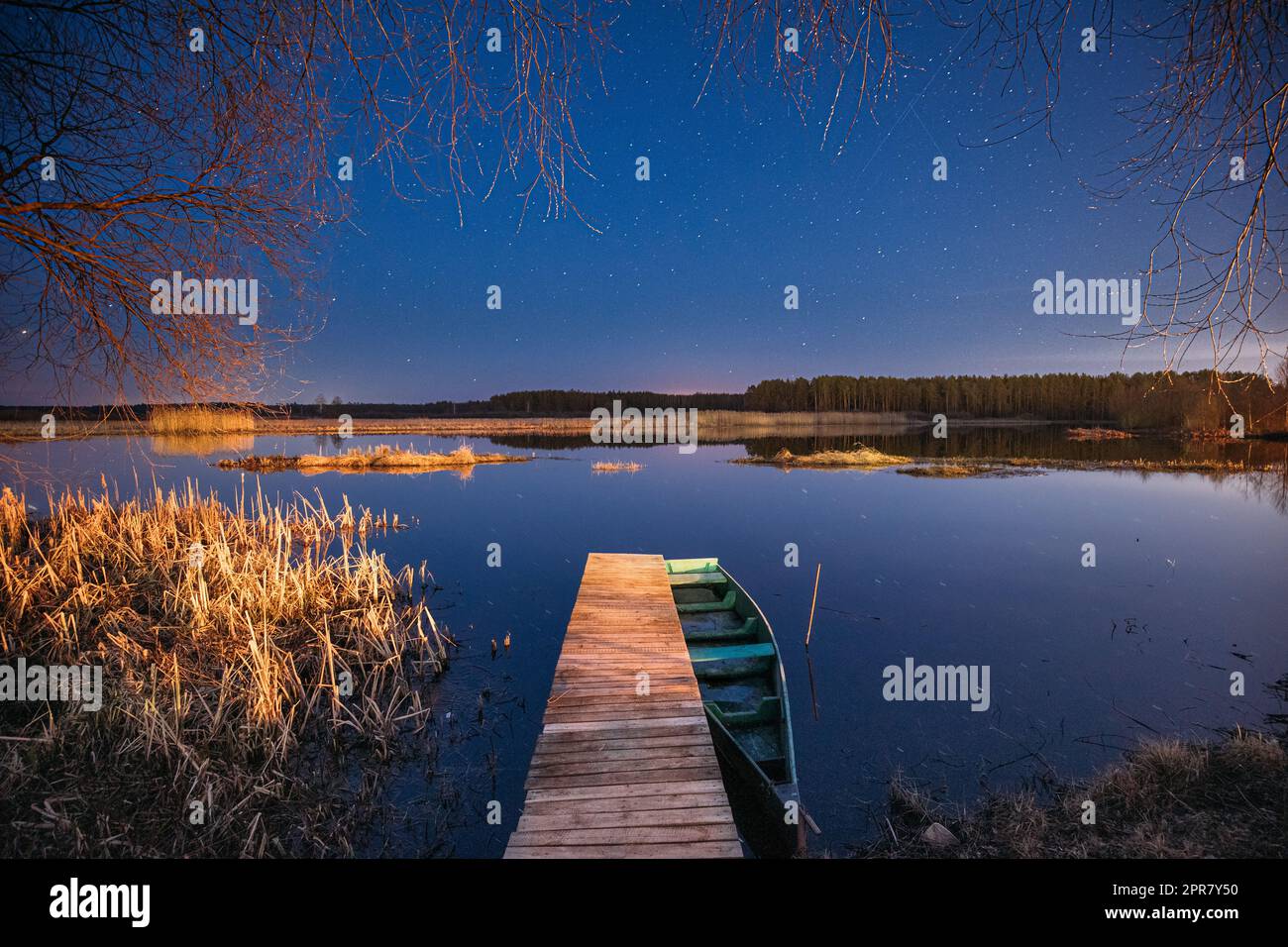 Belarus, Eastern Europe. Real Night Sky Stars Above Old Pier With Moored Wooden Fishing Boat. Natural Starry Sky And Countryside Landscape With Lake River In Early Spring Night. Russian Nature Stock Photo