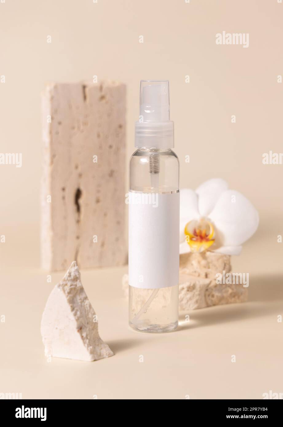 One pump bottle near white orchid flower and stones on light yellow. Mockup Stock Photo