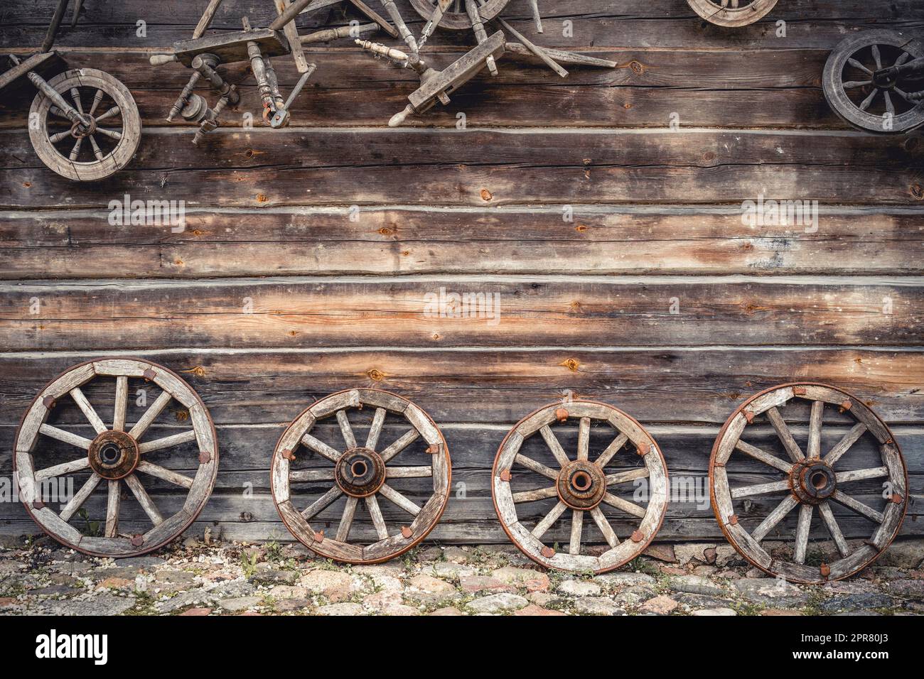 Wooden house wall and ancient wagon wheels, tools and stuff Stock Photo