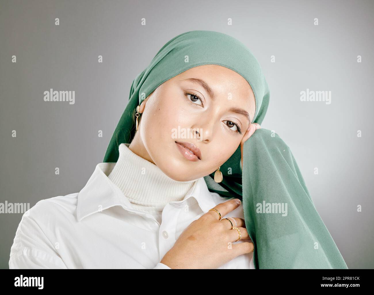 Studio portrait of beautiful muslim woman isolated against a grey background. Young woman wearing hijab or headscarf showing traditional arab modesty holding her hands together and looking at camera Stock Photo