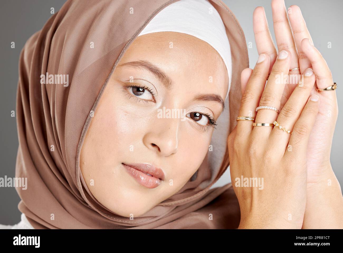 Studio portrait of beautiful muslim woman wearing a brown headscarf and showing multiple rings on her hands. Female wearing hijab and glowing makeup with trendy jewelry showing off her modest beauty Stock Photo